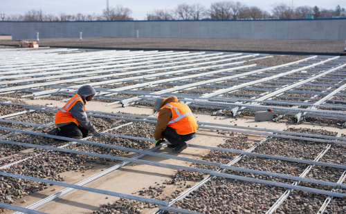 Nicole Hard and Jonathan Aviles, material handlers, from left, align pieces of the racking system for installation of a solar grid on the roof of Repowered in St. Paul. (Alex Kormann/The Minnesota Star Tribune)